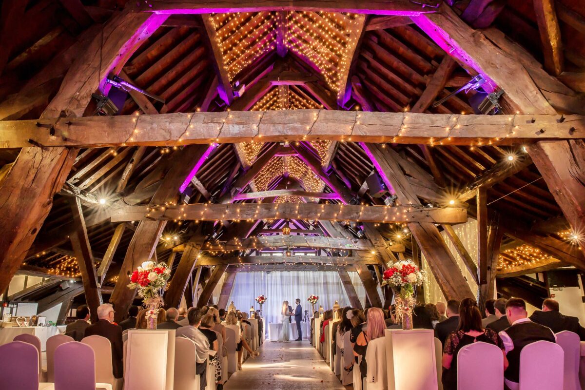 Rustic barn wedding ceremony with decorated ceiling lights.