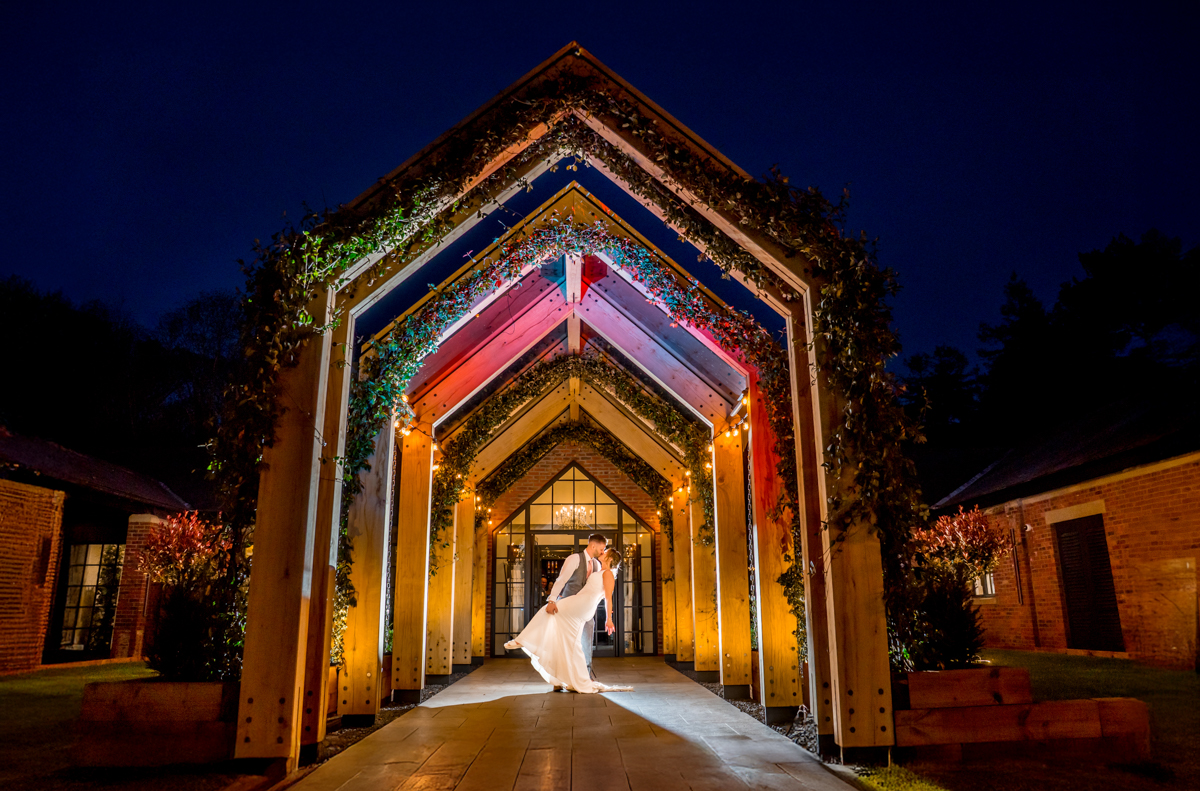 Bride and groom dancing under illuminated archway.