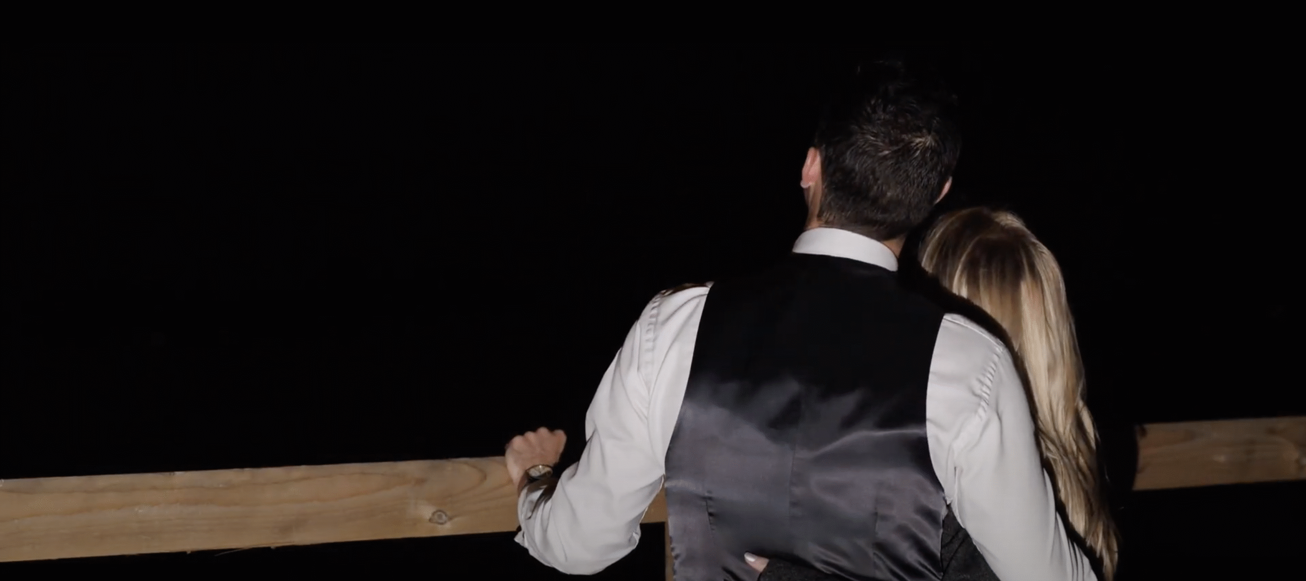 Couple standing together at night on wooden deck.