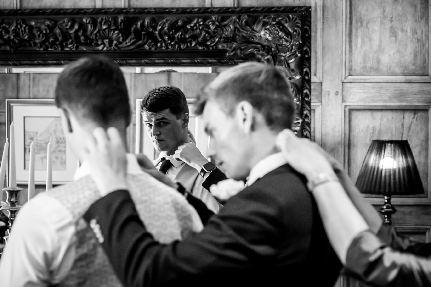 Groom adjusts tie in mirror reflection.