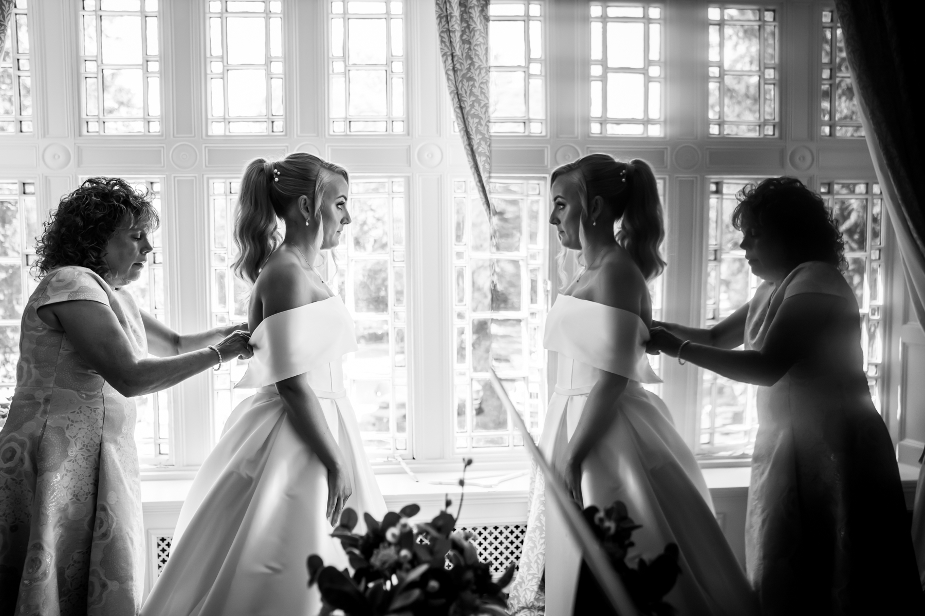 Bride adjusts dress with assistance in elegant room.