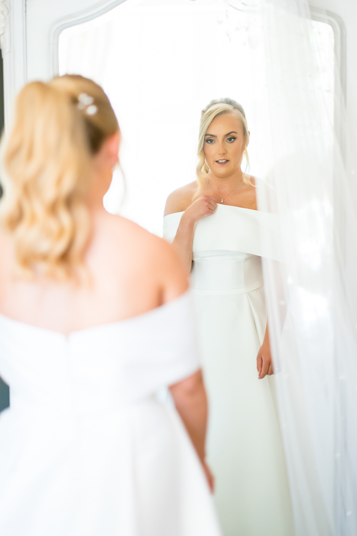Bride in white gown reflected in mirror.