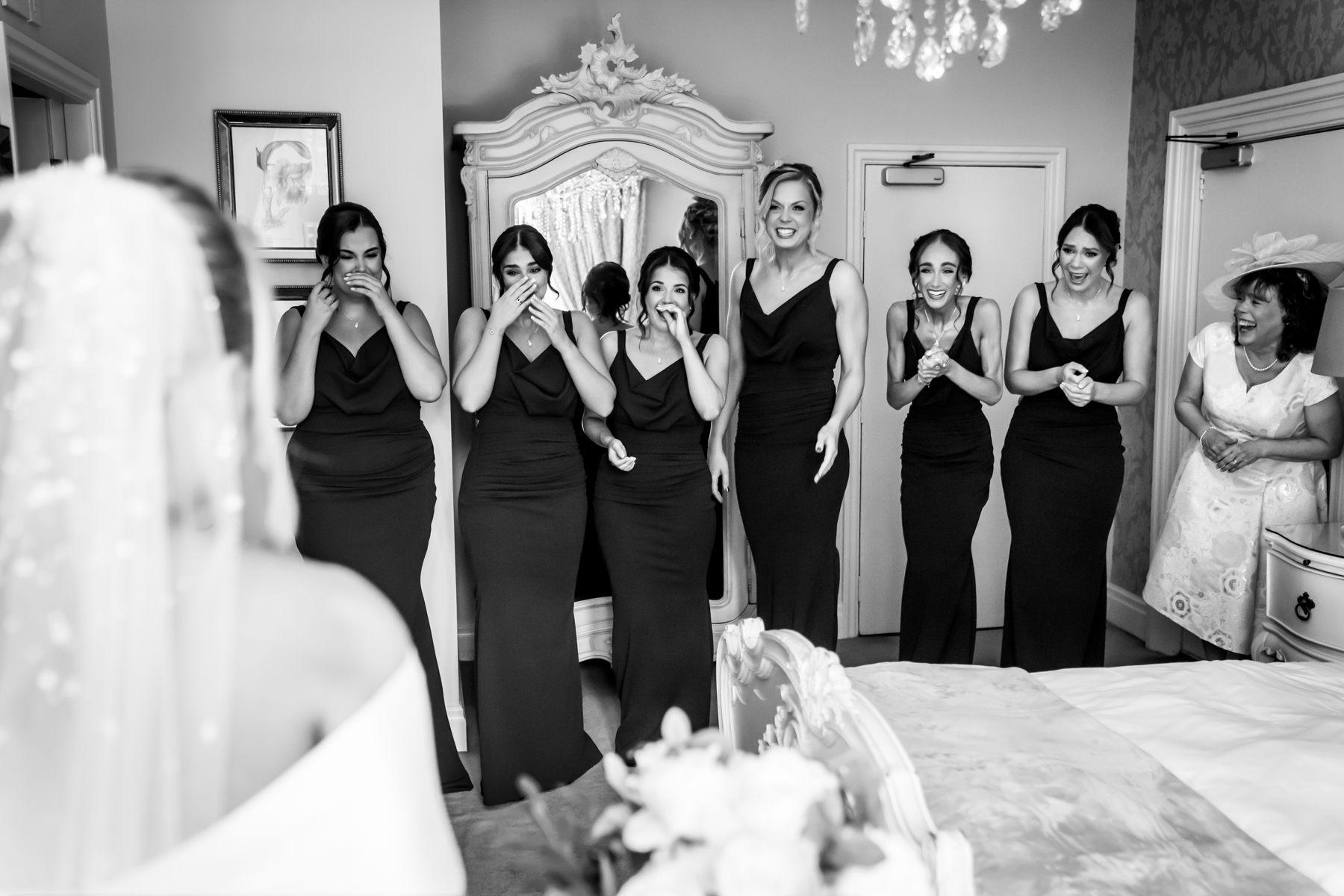 Bridesmaids reacting joyfully to bride in wedding dress.