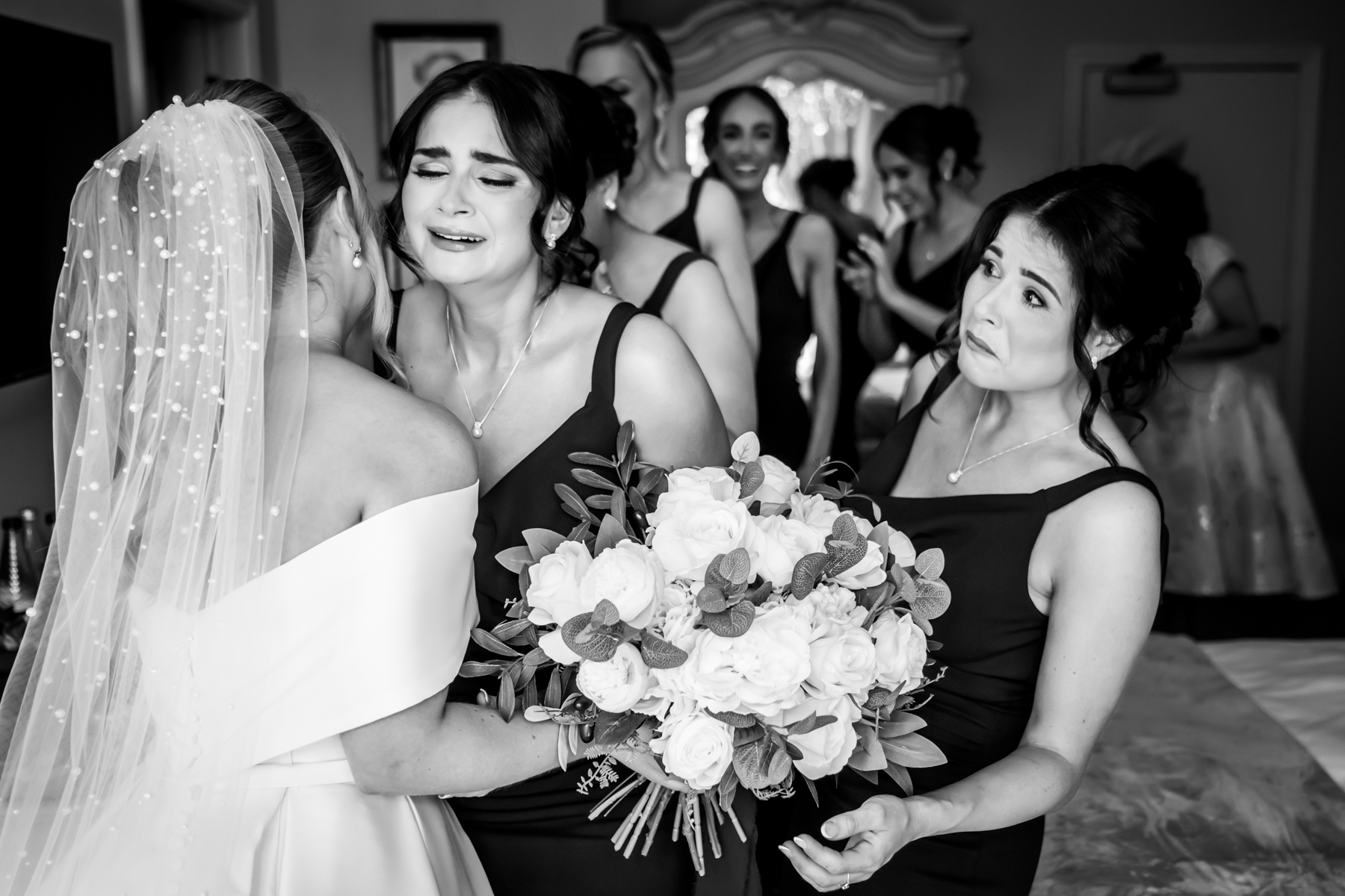 Emotional bridesmaids at wedding with bride in veil.