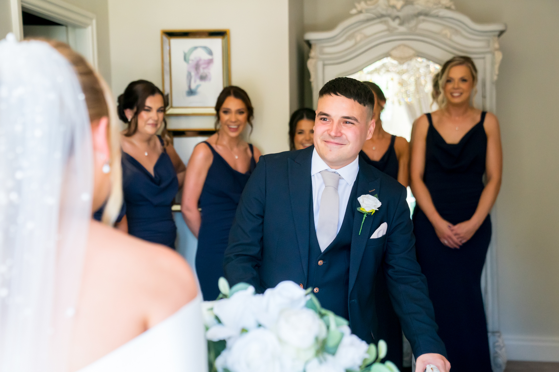 Groom sees bride, bridesmaids smiling in background.
