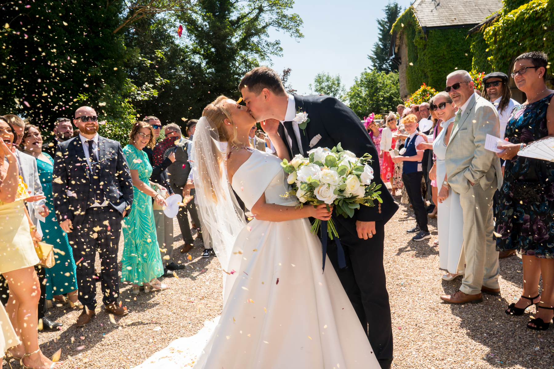 Bride and groom kiss surrounded by guests and confetti.