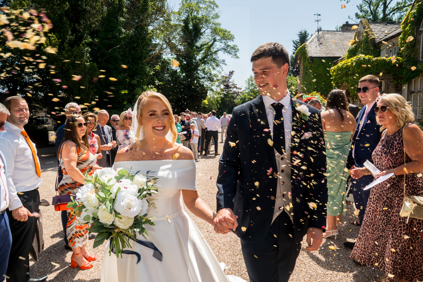 Smiling couple walking through confetti at outdoor wedding.