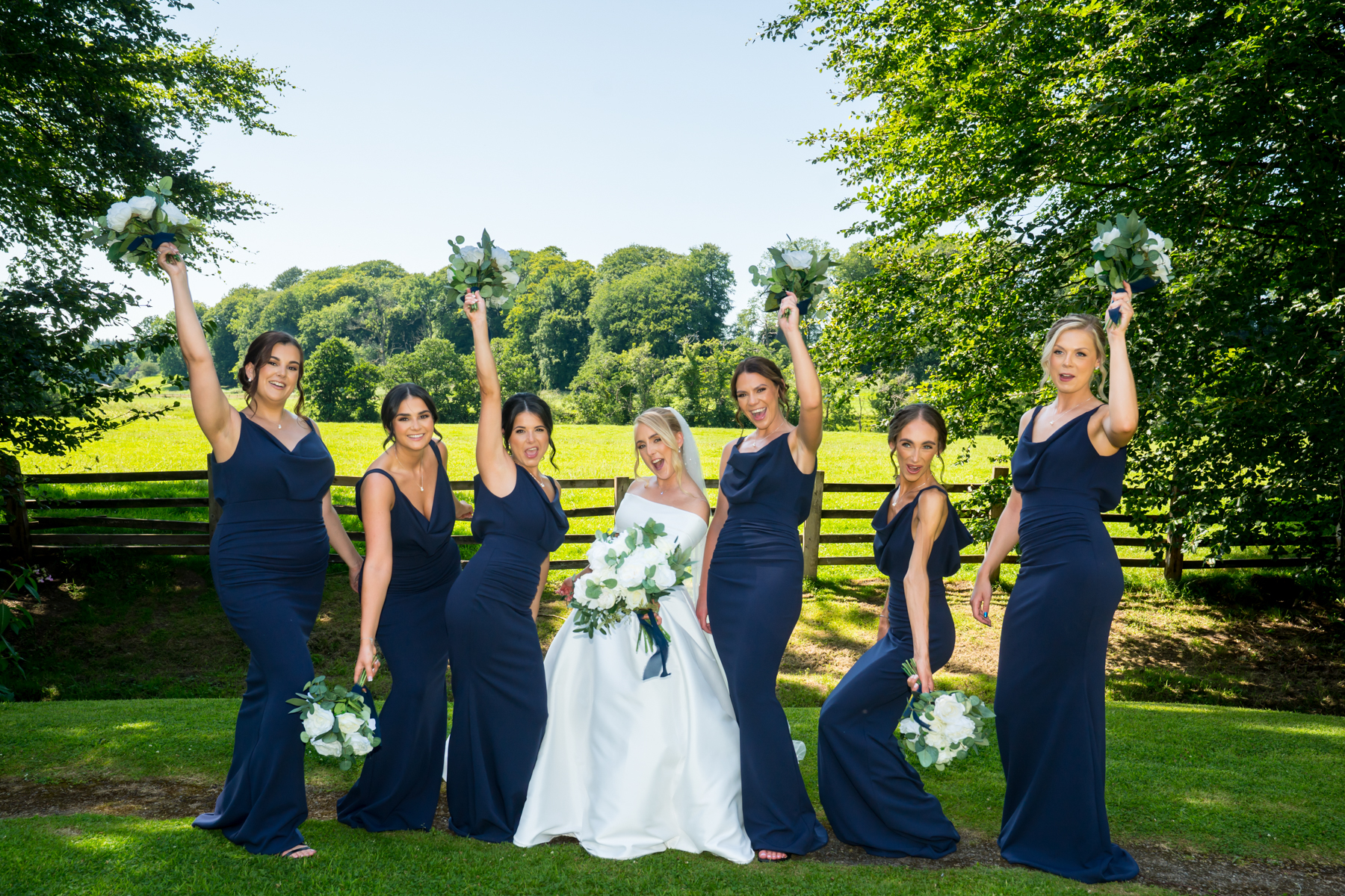 Bride with bridesmaids in navy dresses, holding bouquets.