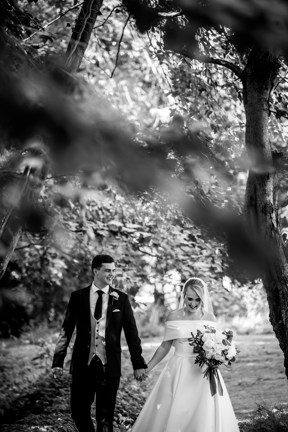 Bride and groom walking in a woodland setting.
