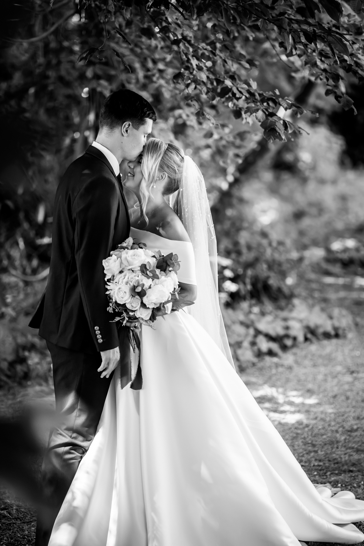 Bride and groom embracing in nature-filled setting.