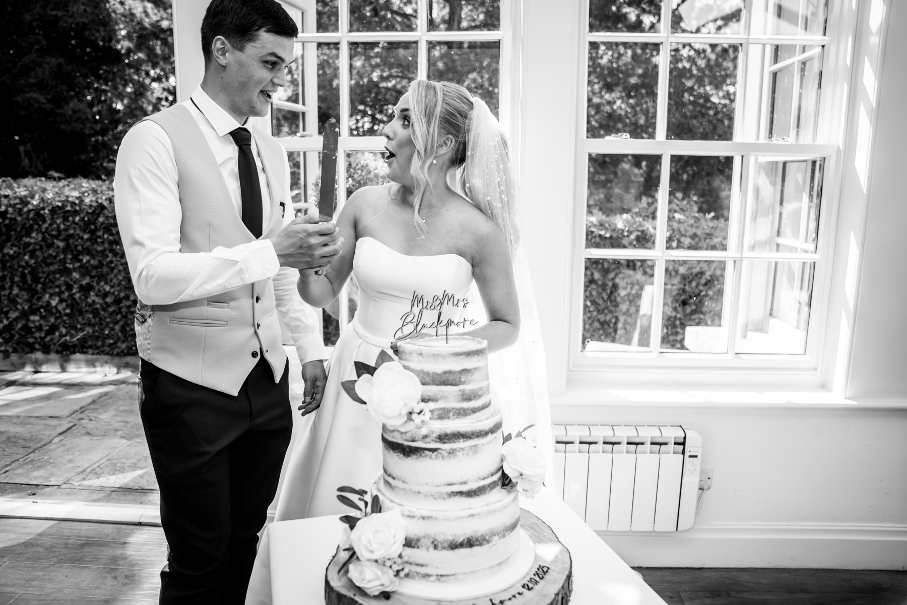 Couple cutting wedding cake together, smiling joyfully.