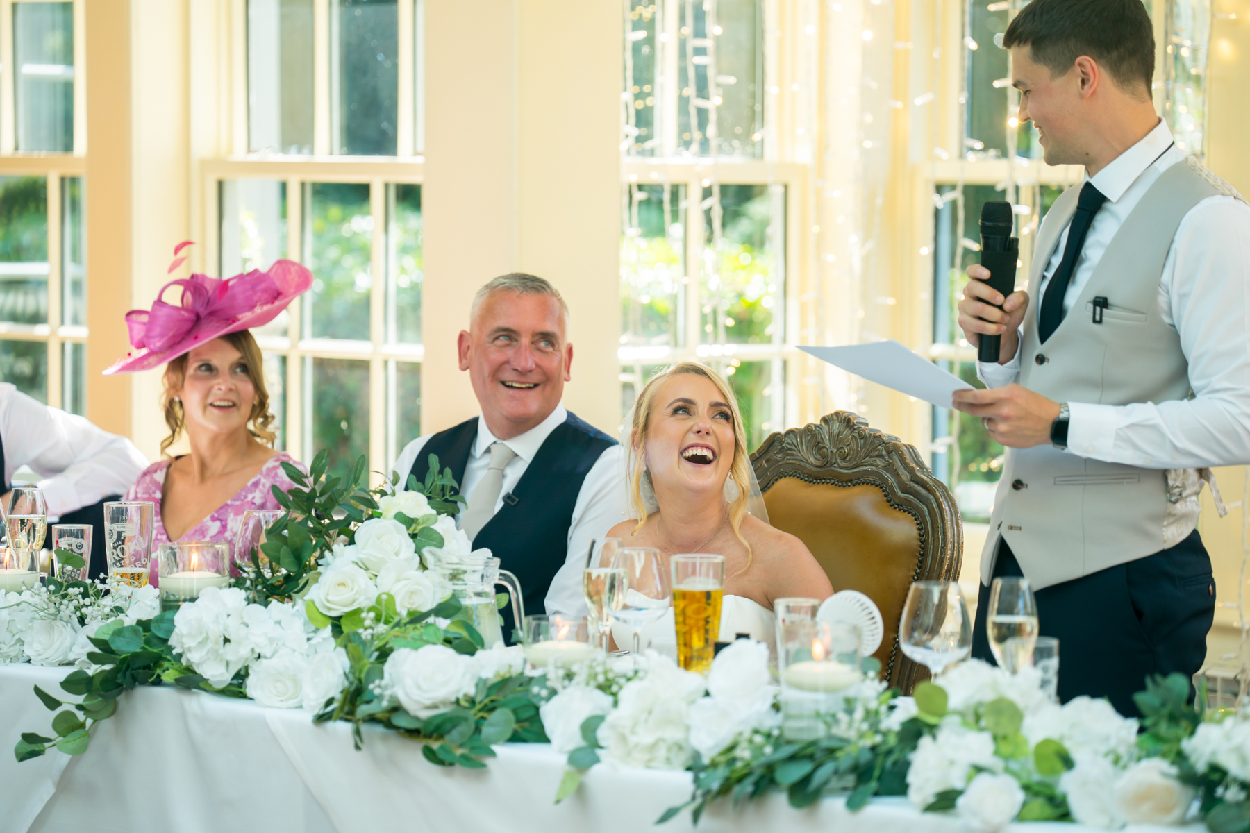 Wedding reception speech with smiling bride and guests.