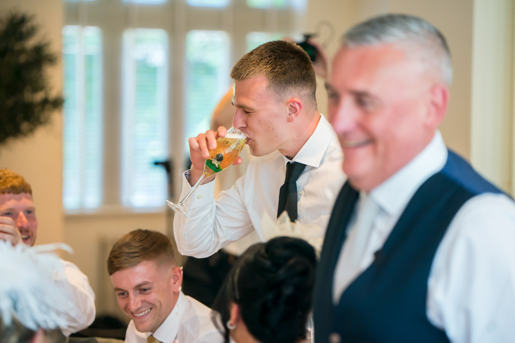 Man in white shirt drinks at wedding celebration.
