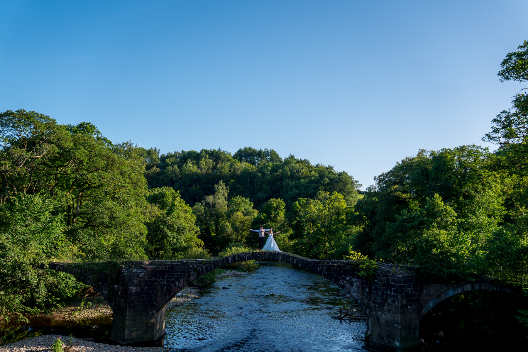 Bride and groom on ancient stone bridge.
