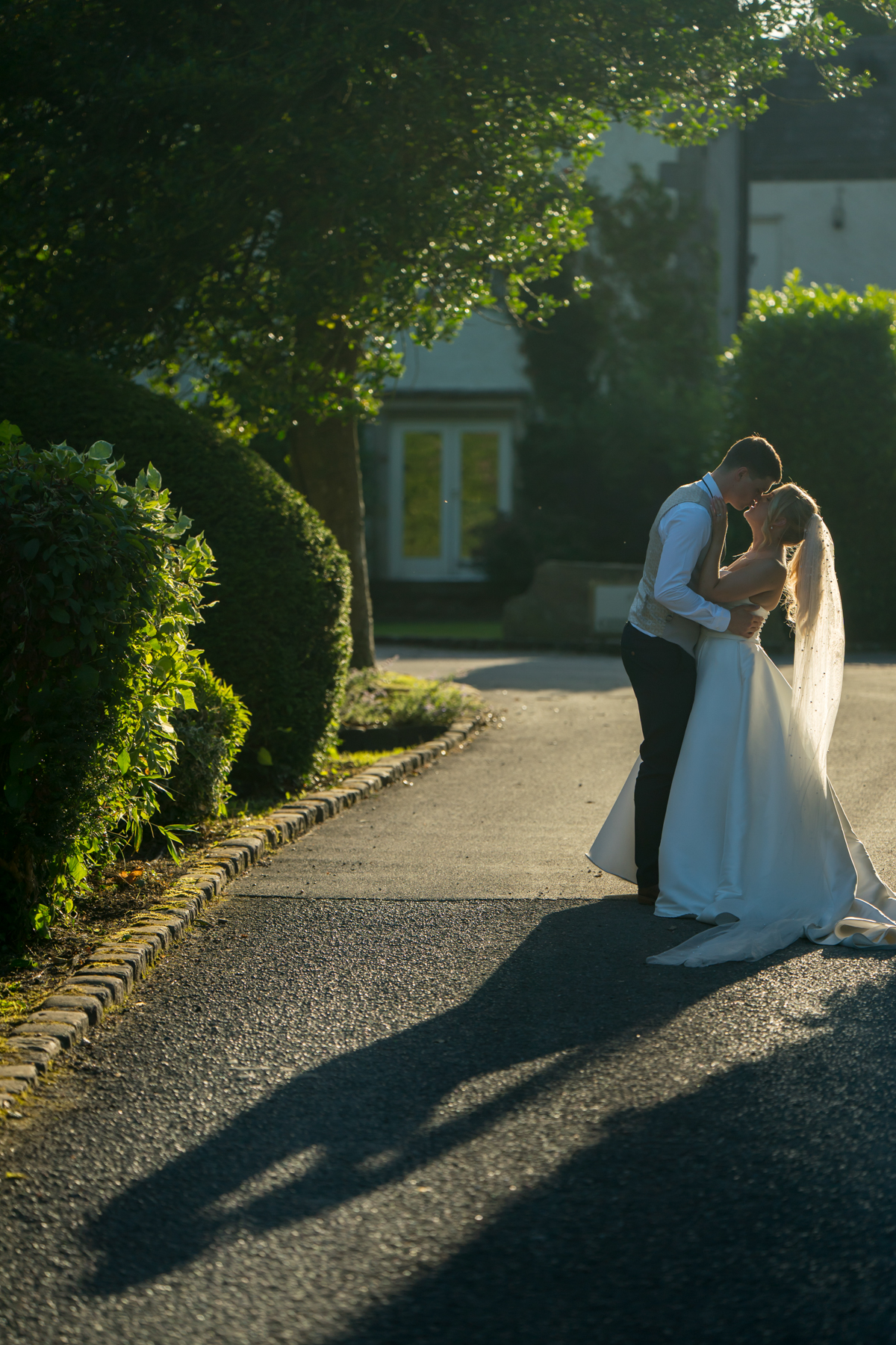 Bride and groom embrace, sunny garden setting.