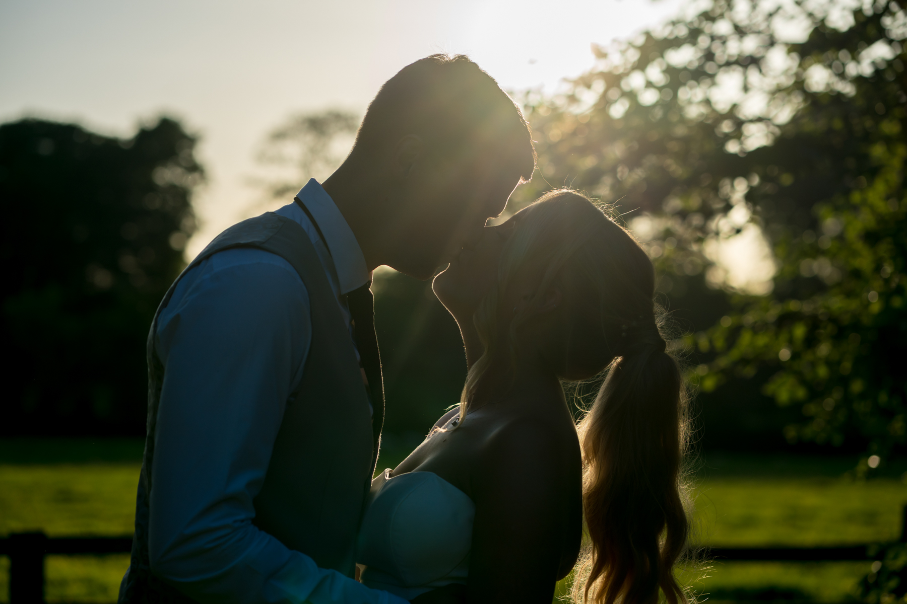 Silhouetted couple kissing at sunset in a field.