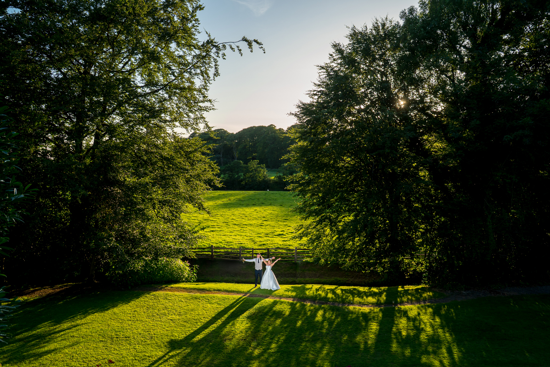 Couple in wedding attire on sunny green field.