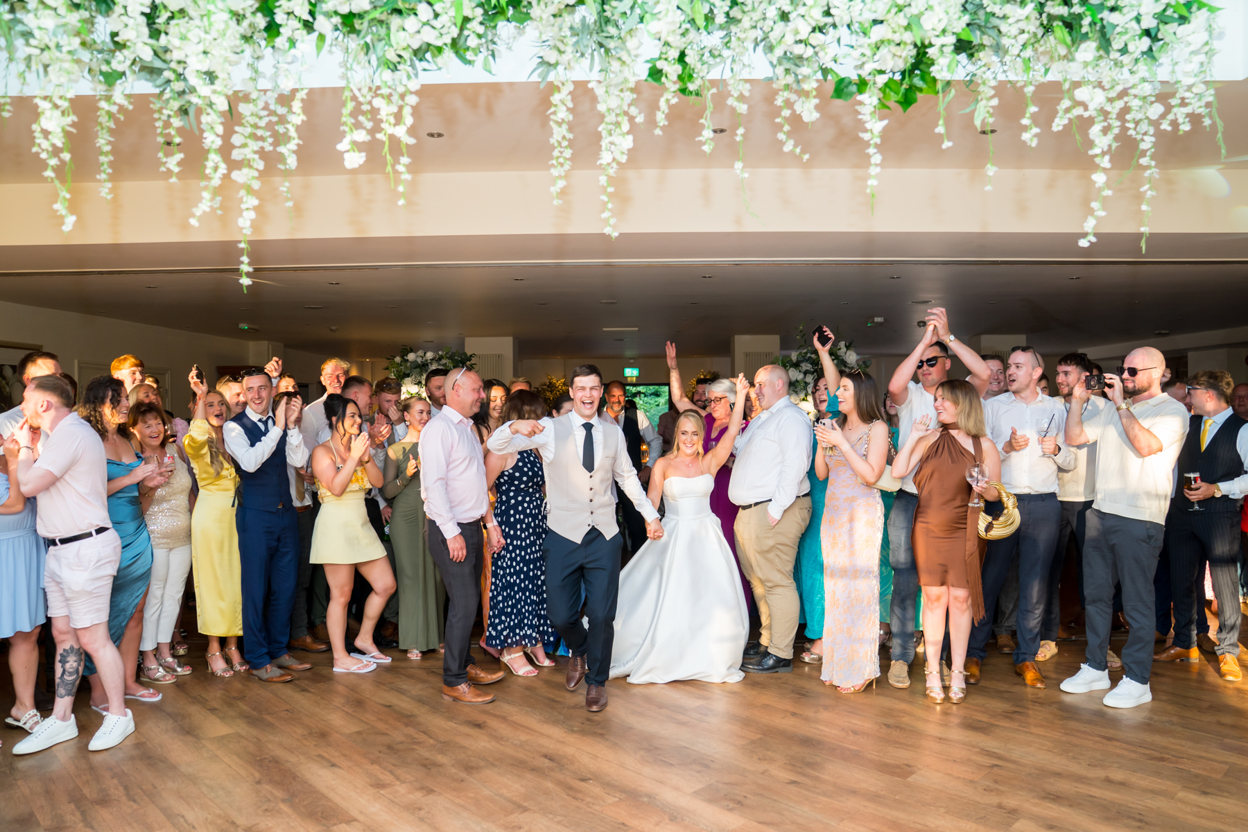 Bride and groom dance, surrounded by cheering guests.