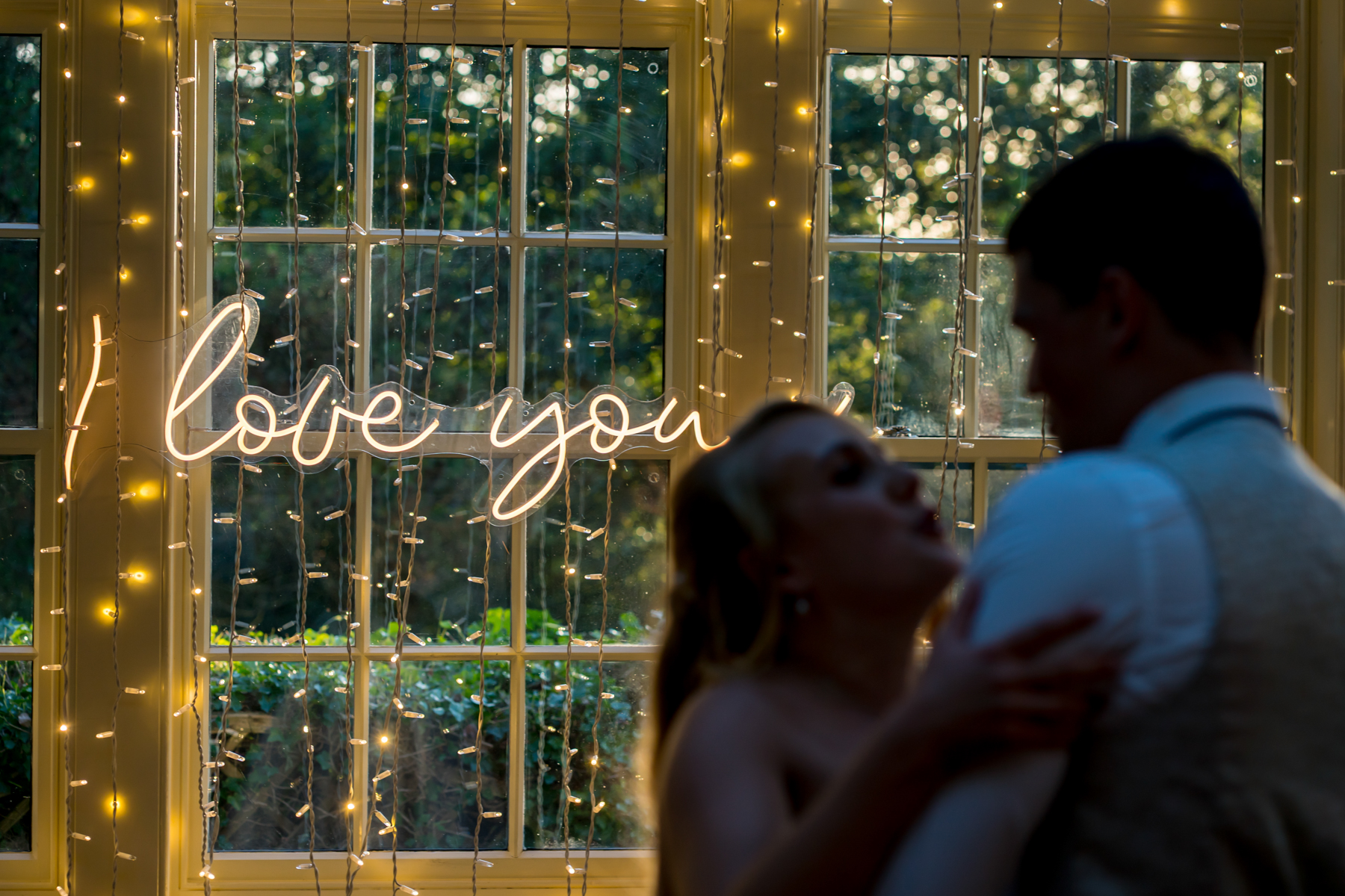 Silhouette couple dancing, illuminated 'I love you' sign.