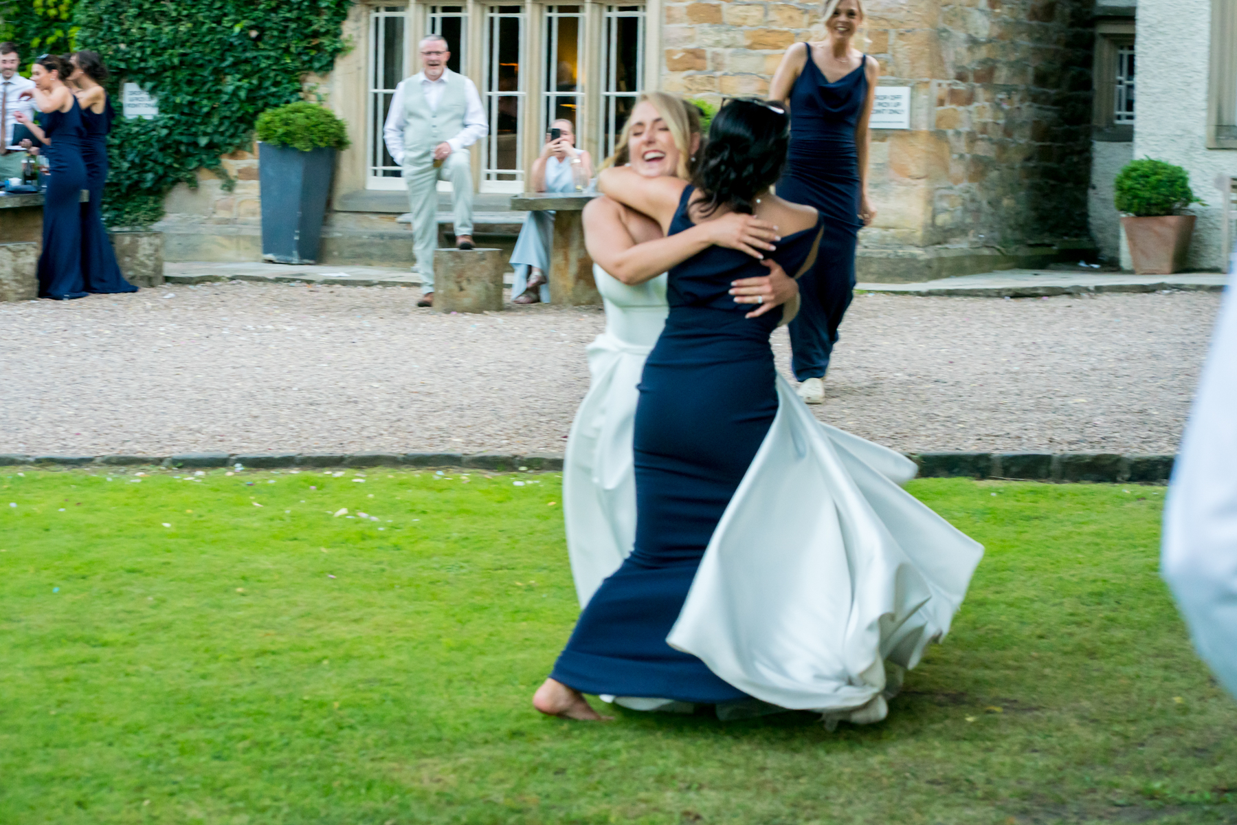 Two women hugging at outdoor wedding reception.