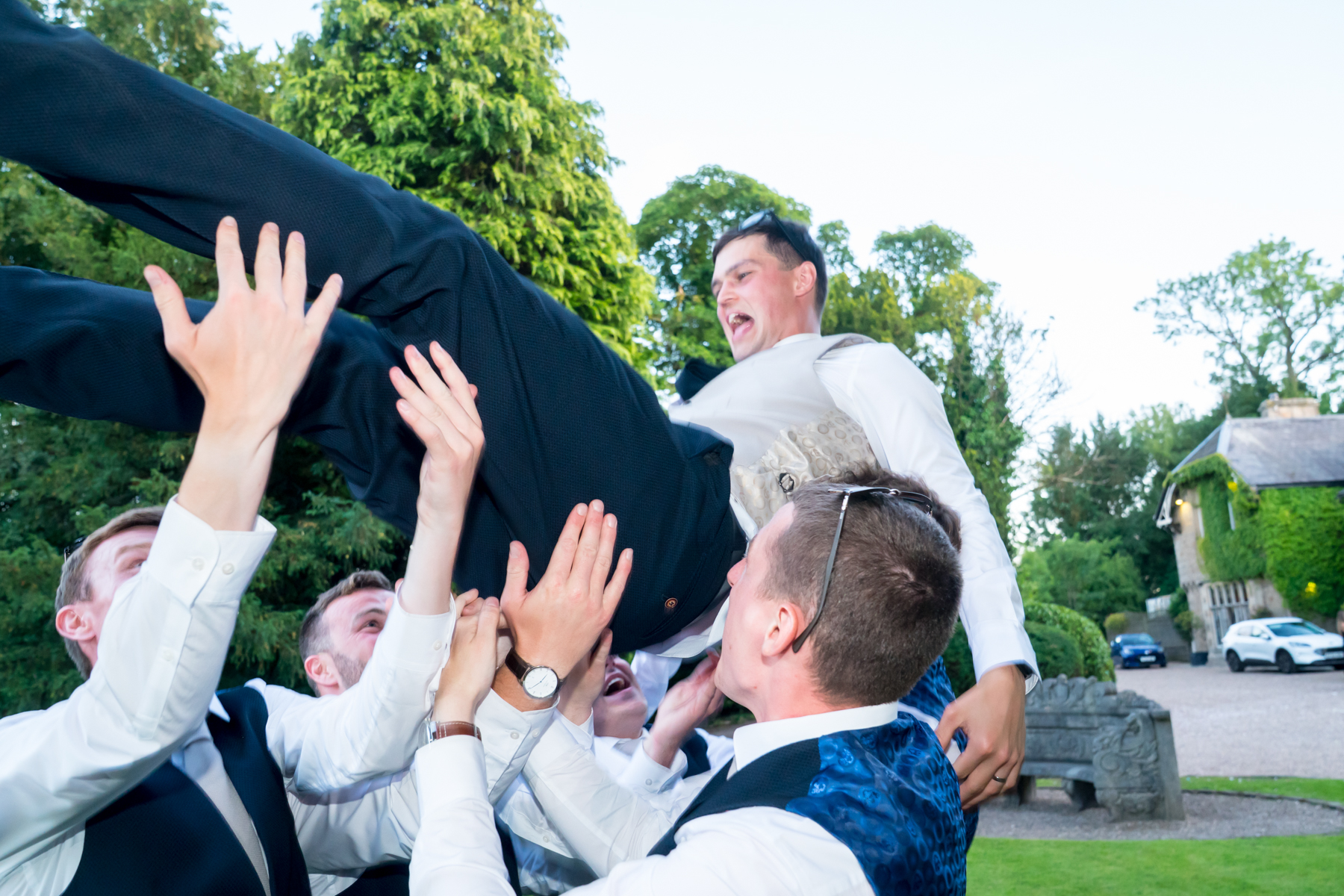Friends joyfully lift man during outdoor celebration.