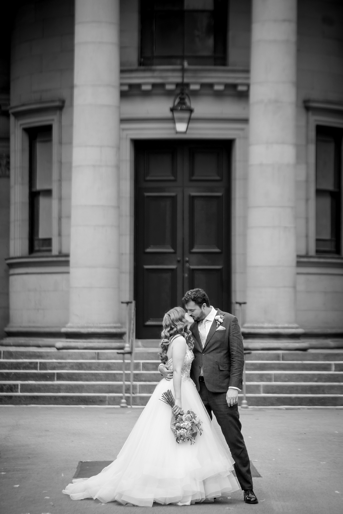Bride and groom kiss outside classic building.