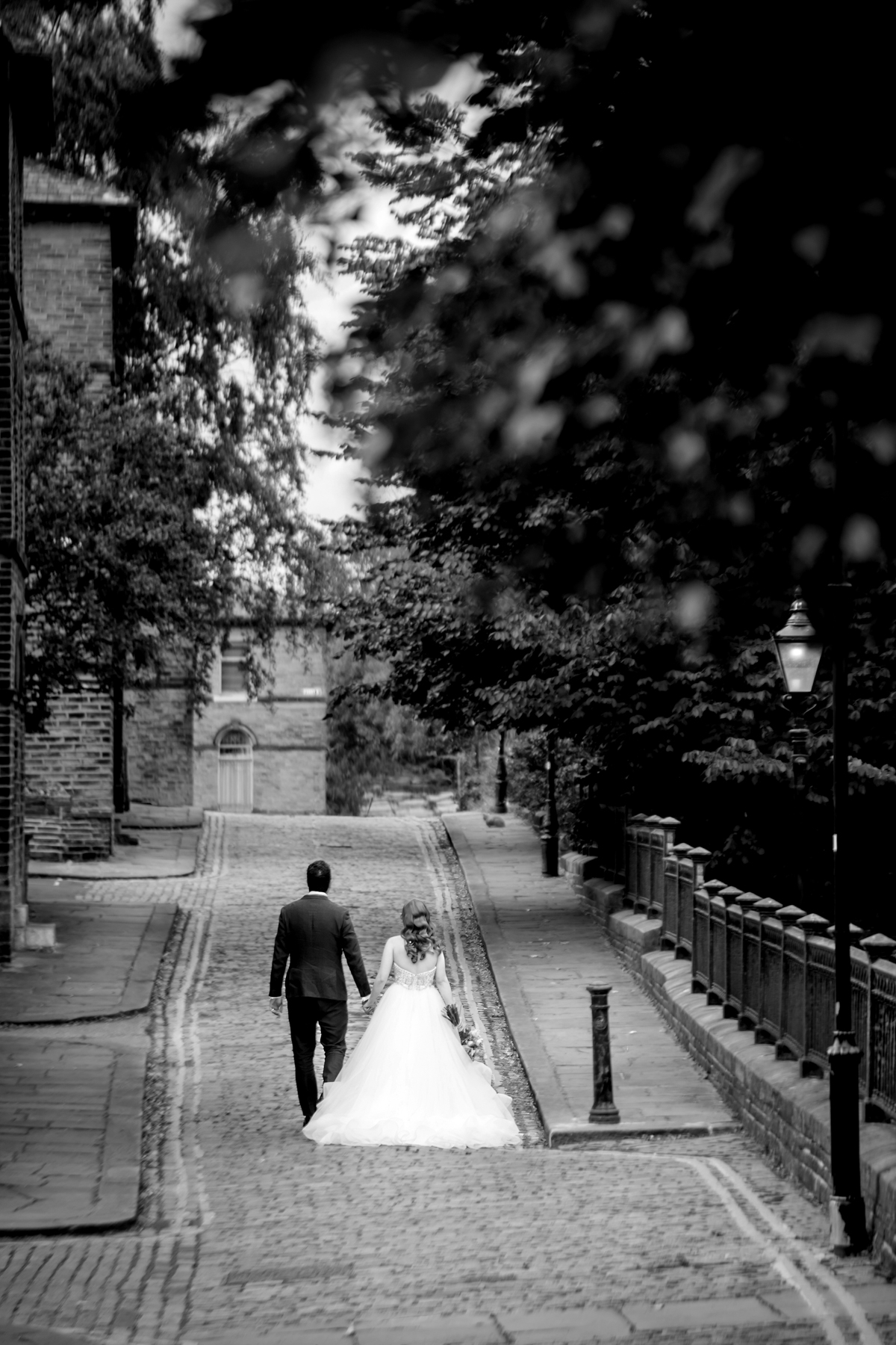 Bride and groom walk down cobblestone path.