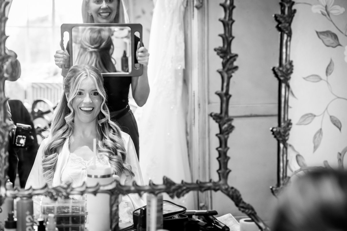 Bride admires hairstyle in ornate salon mirror.