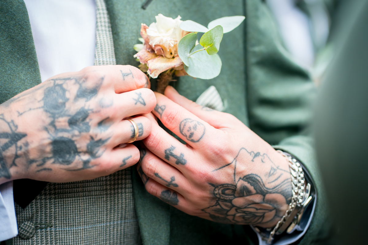 Tattooed hands adjusting boutonniere on suit jacket.