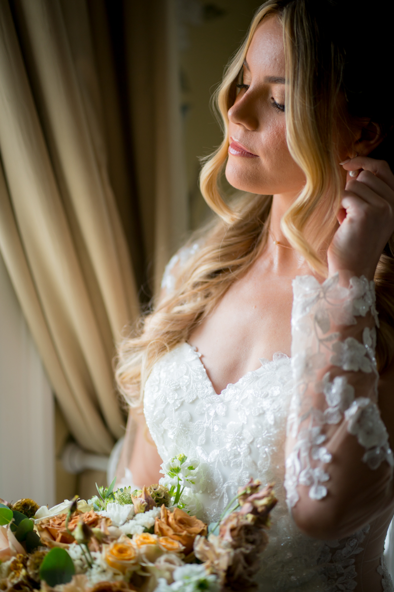 Bride holding bouquet near window with closed eyes.