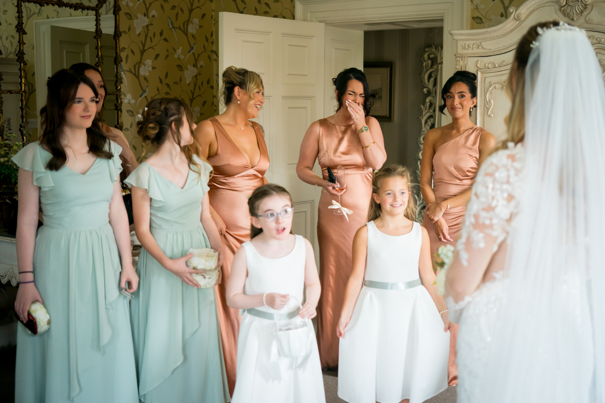 Bridesmaids and flower girls admire bride in wedding dress.