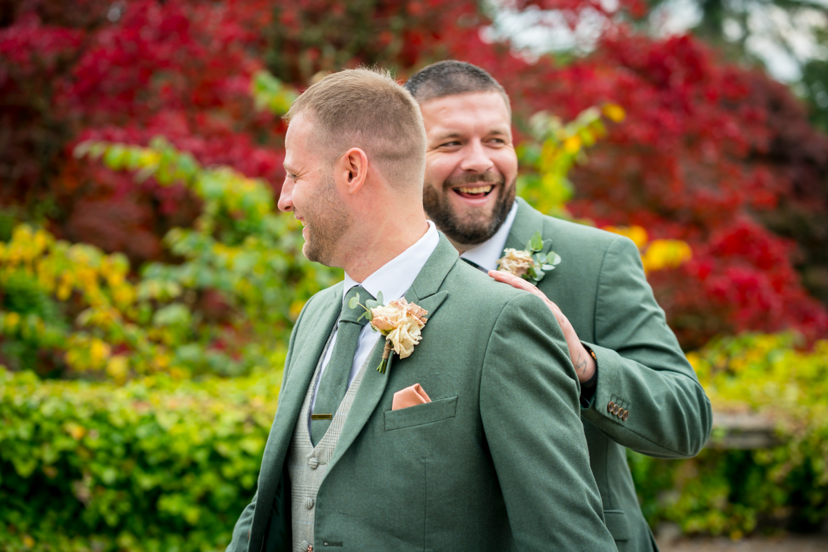 Two men in green suits laugh outdoors.