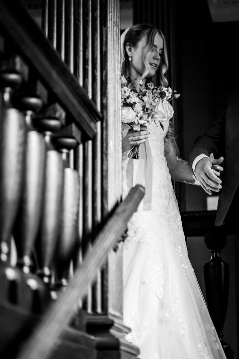 Bride descending staircase holding bouquet, black and white.