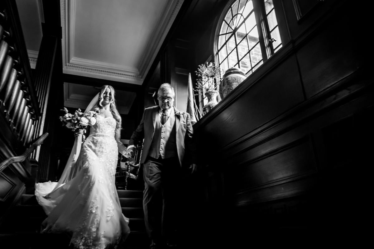 Bride and father descending staircase elegantly.