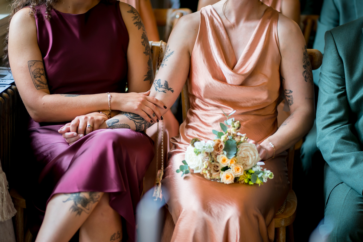 Two women in dresses holding hands at event.