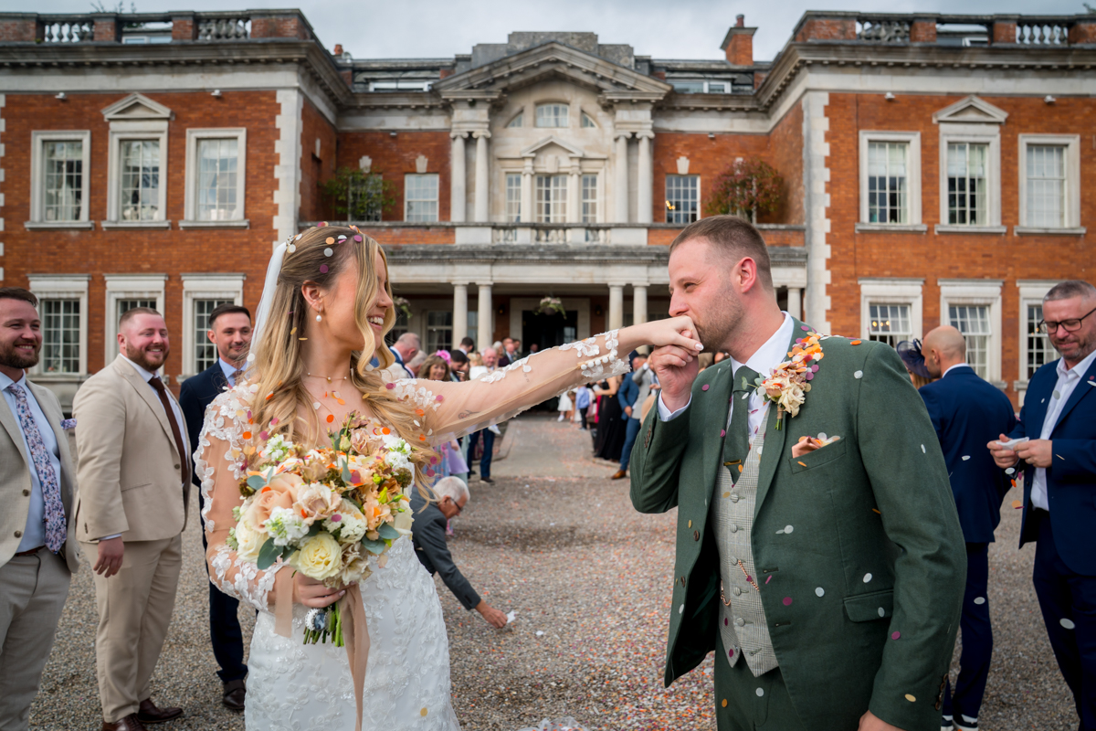 Bride and groom kissing hand outside mansion