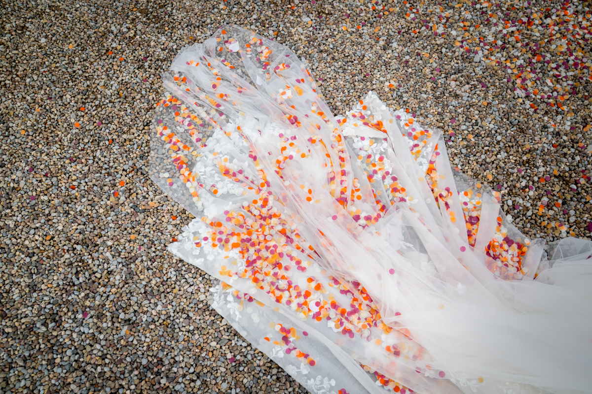 White wedding veil covered in colourful confetti on gravel.