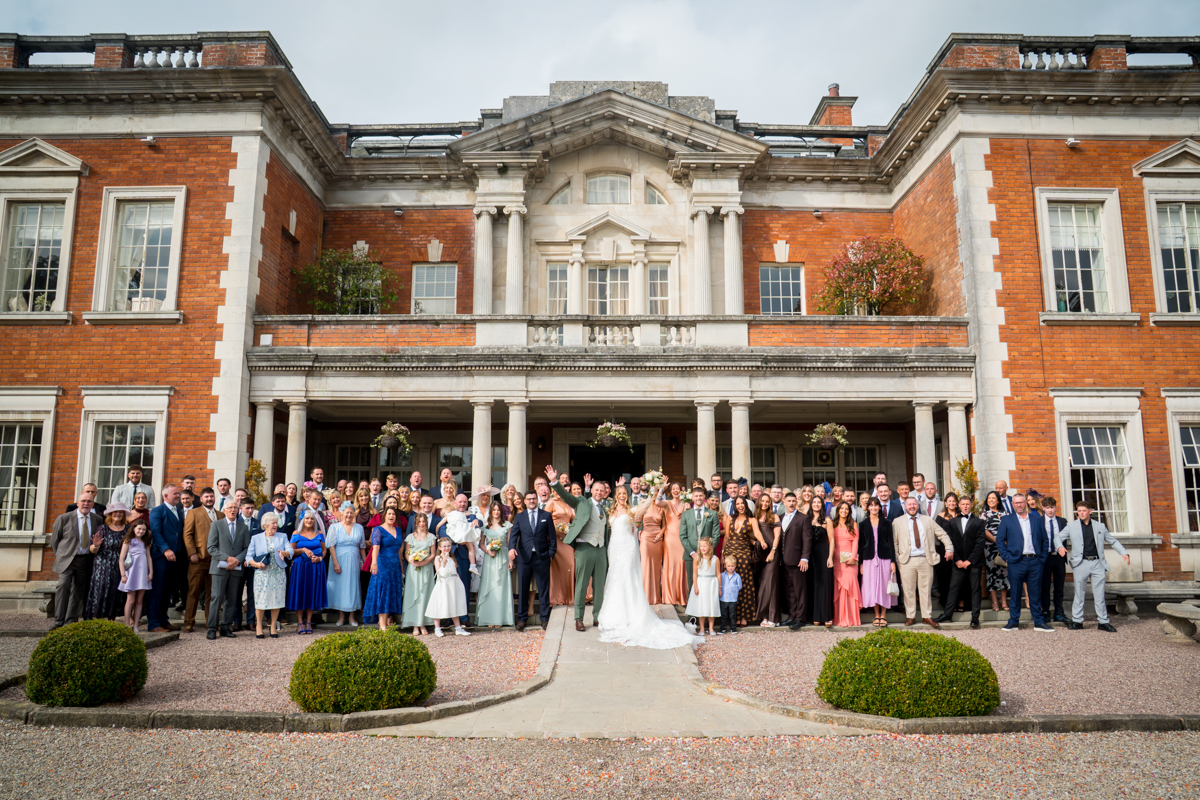Large wedding group outside historic manor house.