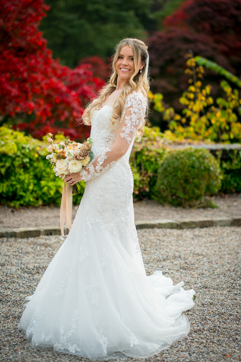 Bride in white gown holding bouquet outdoors.
