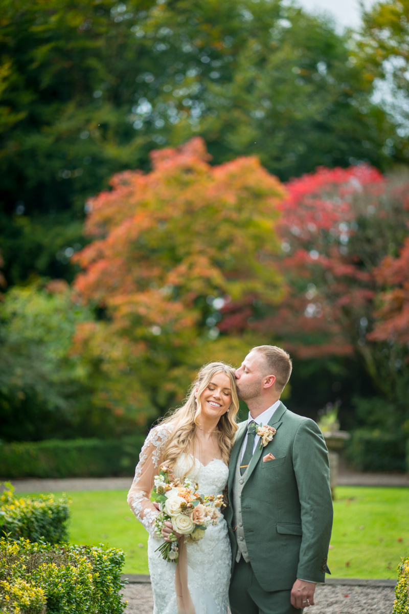 Bride and groom in garden with autumn leaves.