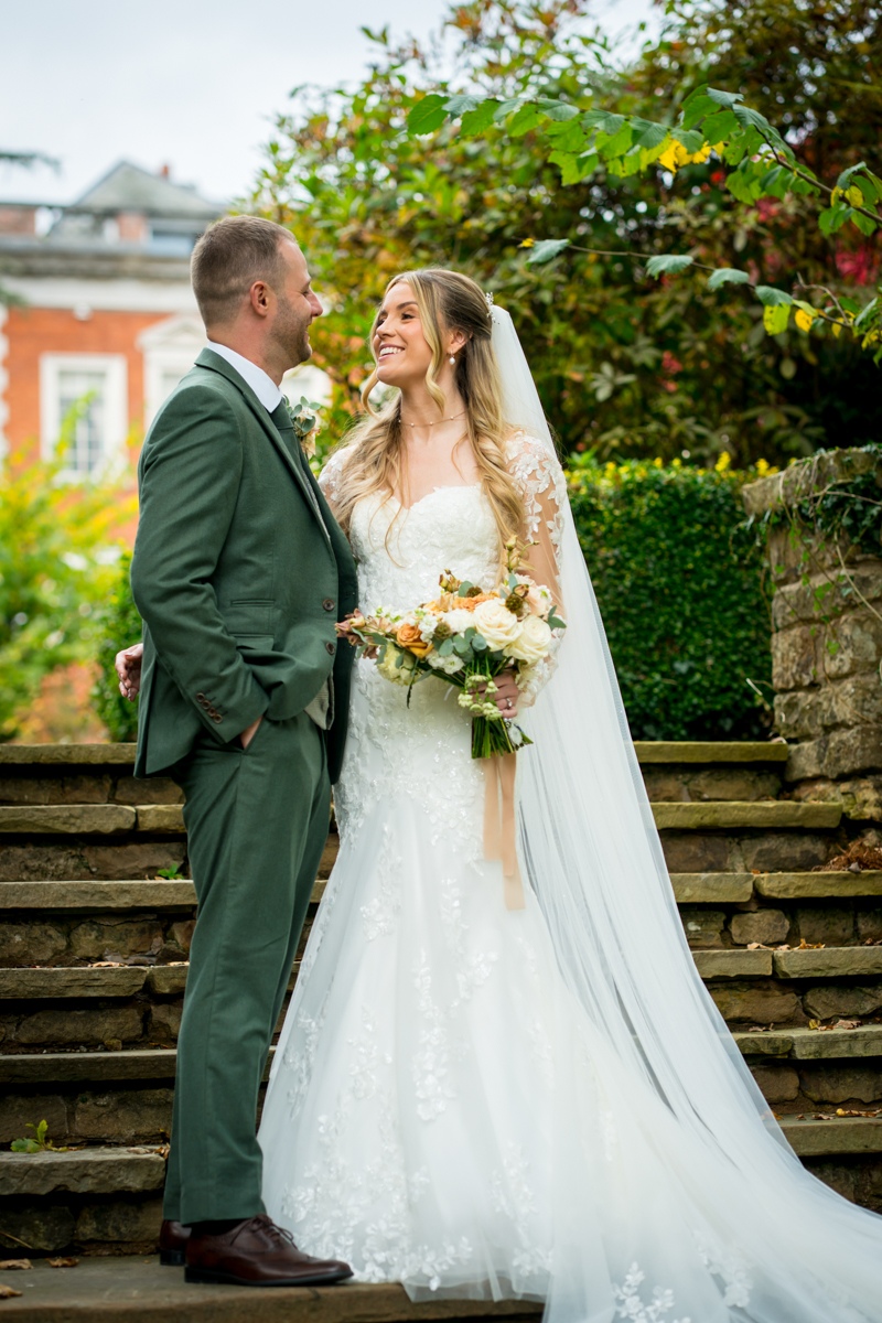 Bride and groom smiling on garden steps.