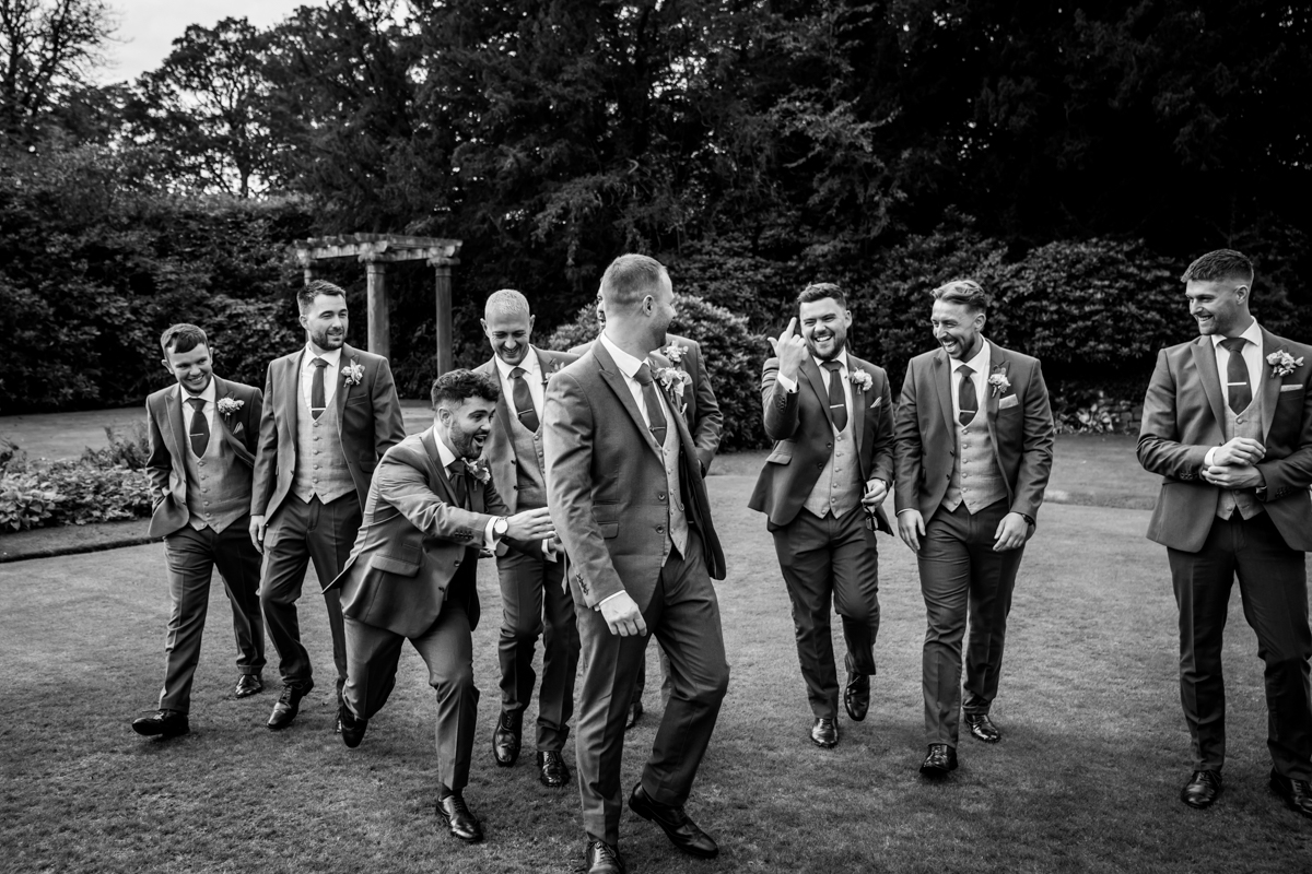 Groom and groomsmen laughing in garden setting.
