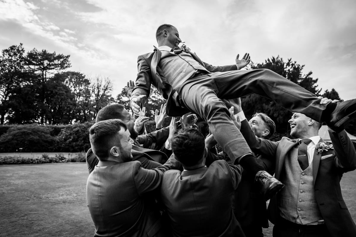 Joyful groomsmen lifting groom in celebration.