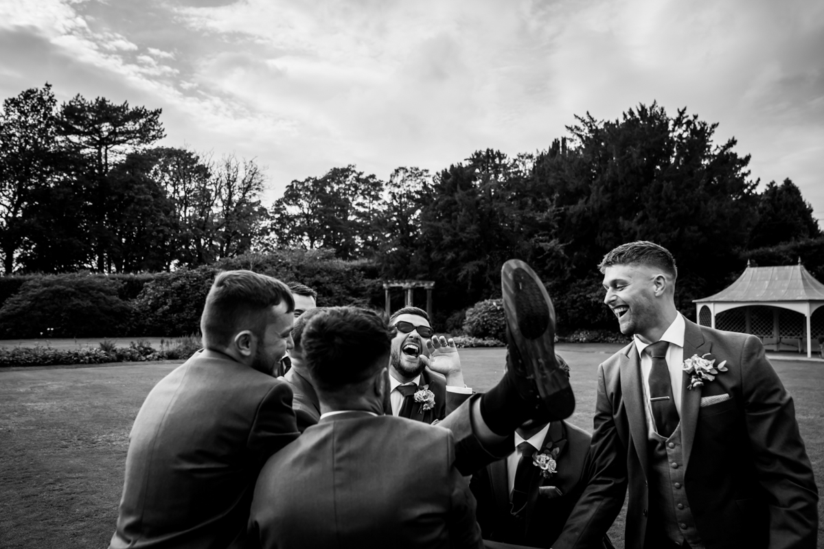 Groomsmen laughing and lifting a friend at wedding.