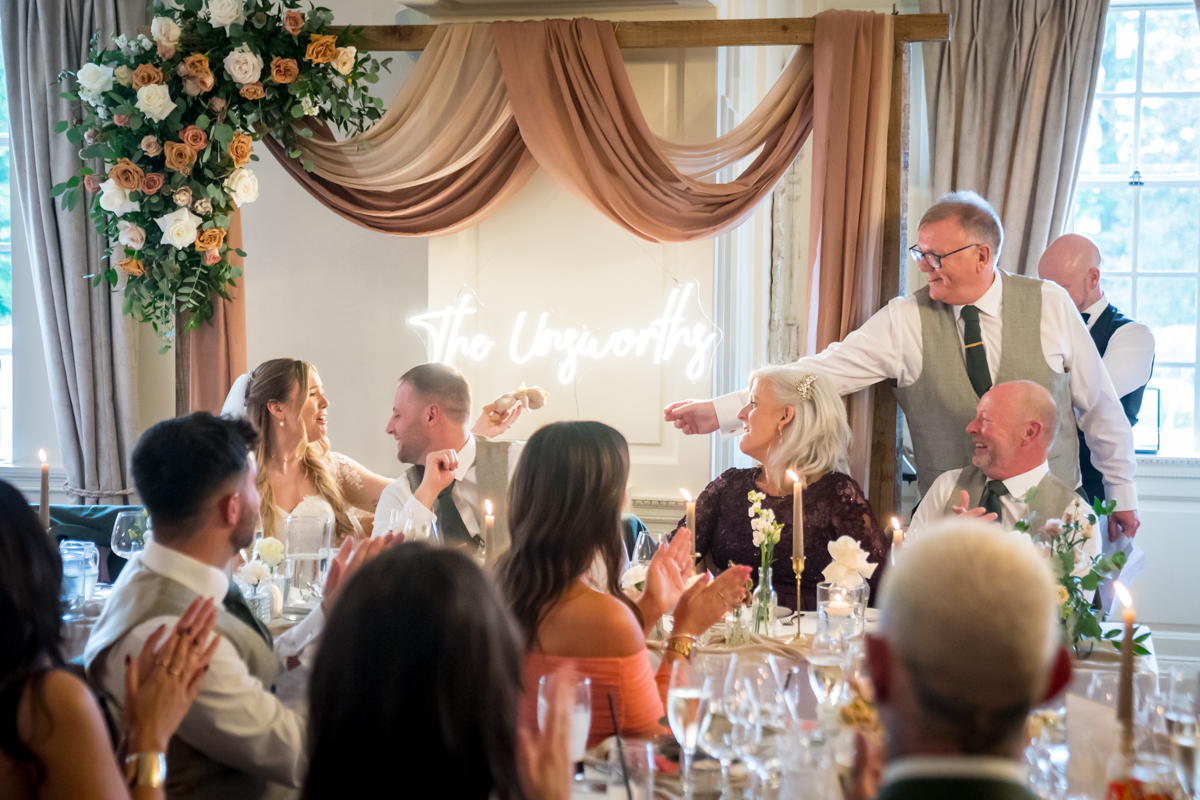 Wedding speech with guests applauding, floral decor visible.
