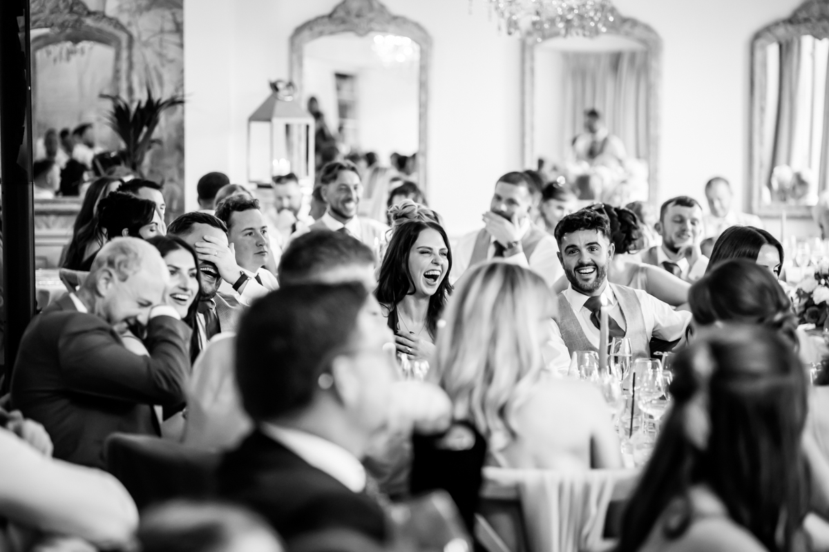 Guests laughing at wedding reception in black and white.
