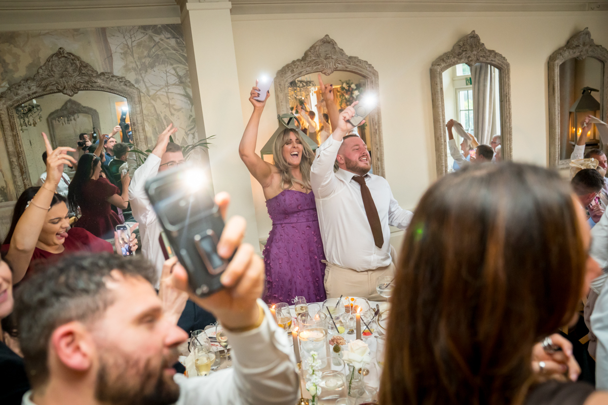 Guests celebrating with phones and lights at reception.