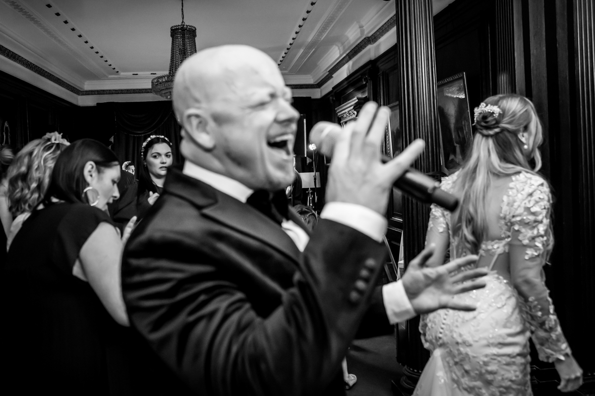 Man singing at a formal event, black and white.