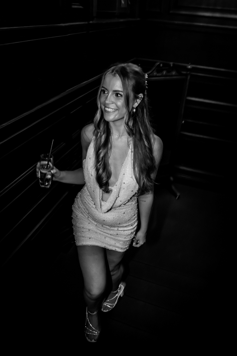 Woman in elegant dress with drink, smiling.