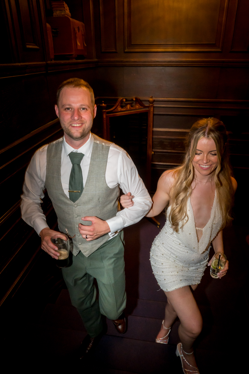 Couple ascending stairs at stylish event, holding drinks.